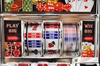A close-up view of a slot machine with vibrant colors and various gambling symbols such as dice, coins, and playing cards. The reels display a combination of symbols, including bars, cherries, and the number seven. The chrome exterior and colorful details convey the theme of casino and gambling.