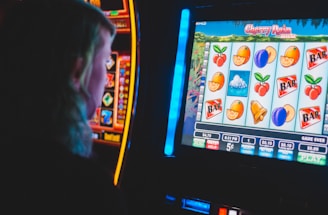 A person is closely observing a digital slot machine with colorful fruit symbols, bars, and a bell. The slot machine screen displays symbols like oranges, plums, cherries, and clouds. The background is dimly lit, creating a focused and somewhat intense atmosphere.