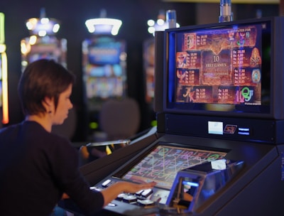 A person is seated at a slot machine console in a casino, focusing intently on the game displayed on the screen. The background shows several other illuminated gaming machines, adding a vibrant and colorful atmosphere to the scene.